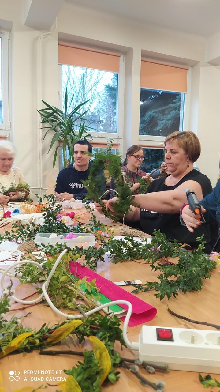Widać uczestników warsztatów podczas zdobienia wianków gałązkami bukszpanu.
