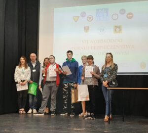 Grupa finalistów  z dyplomami oraz Pani wicedyrektor z organizatorami na na scenie auli.