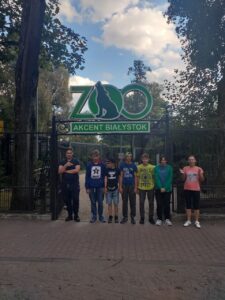 Siedem osób stoi przed wejściem do ZOO, za nimi napis ZOO Akcent Białystok