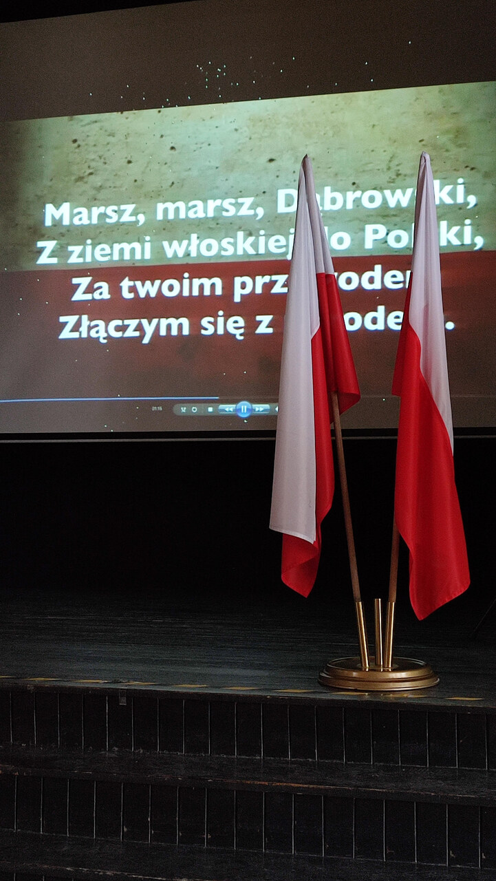 Polskie flagi, w tle ekran z tekstem hymnu