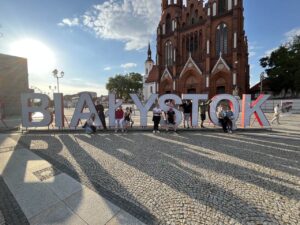 uczestnicy spaceru stoją przy wielkim napisie Białystok, w tle znajduje się Katedra