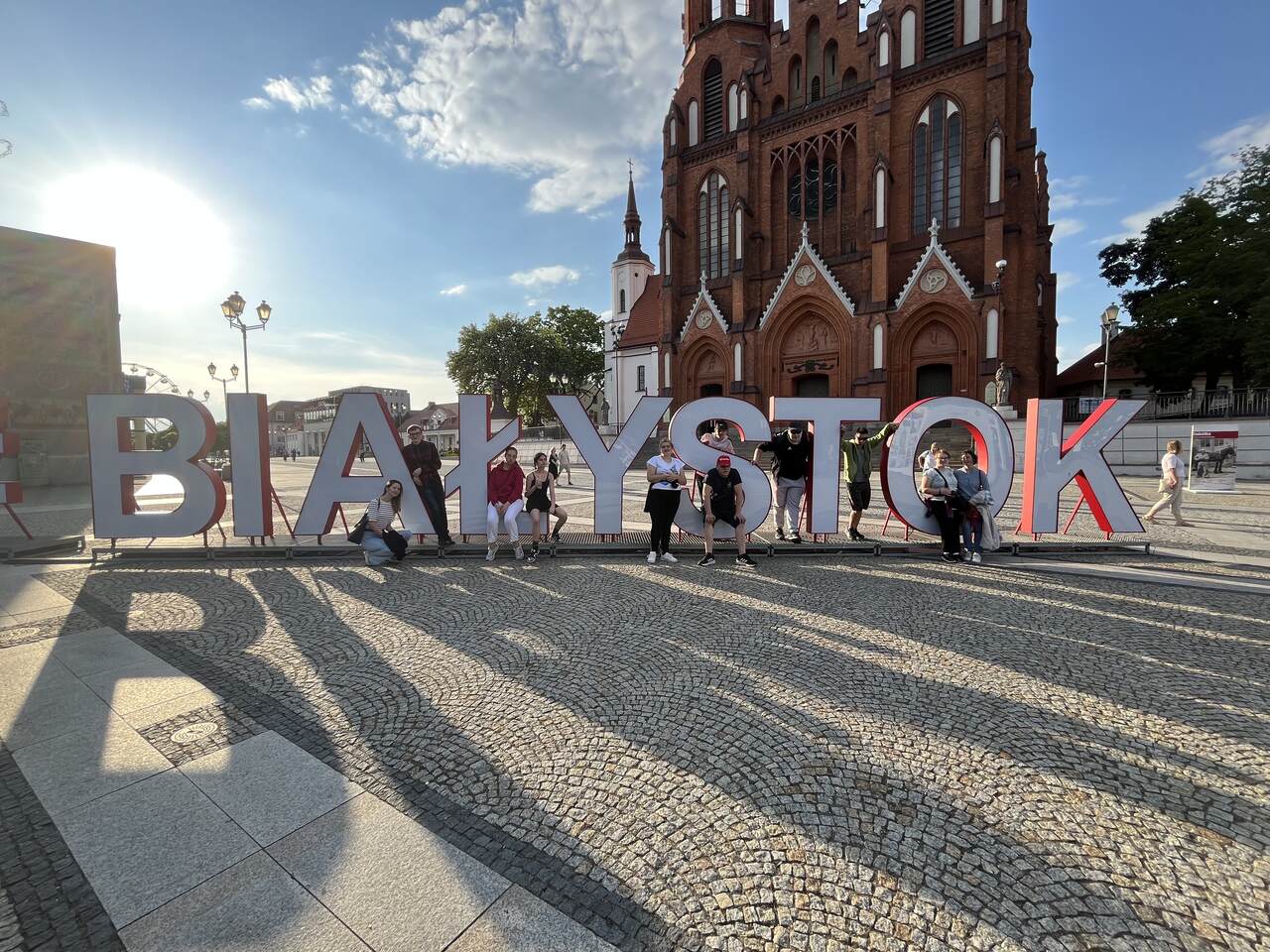 uczestnicy spaceru stoją przy wielkim napisie Białystok, w tle znajduje się Katedra