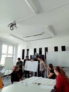 Czterech chłopców stojąc przed klasą prezentuje swoją pracę na dużym arkuszu papieru.