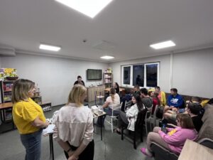 Wychowankowie siedzą na krzesłach, Panie prowadzące wprowadzają wychowanków w temat zajęć.
