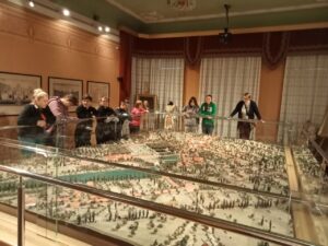 Młodzież wraz z wychowawcą patrzą na wielką makietę miasta w muzeum.