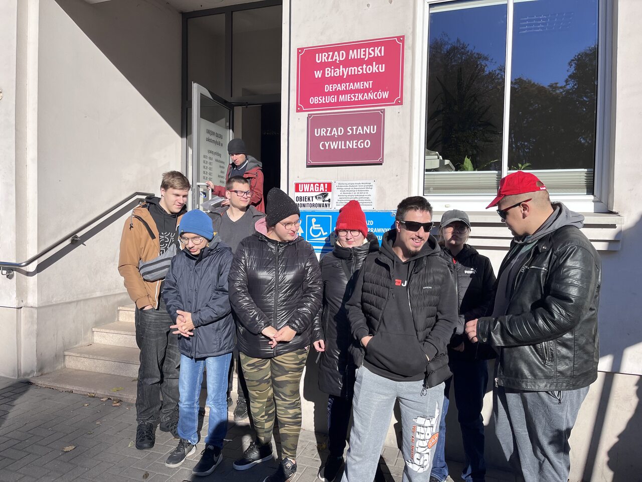 Młodzież stoi przed budynkiem Urzędu Miejskiego.
