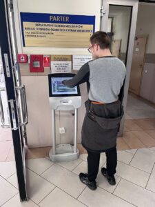 Wychowanek stoi przy monitorze, gdzie wybiera, którą sprawę urzędową chce załatwić.
