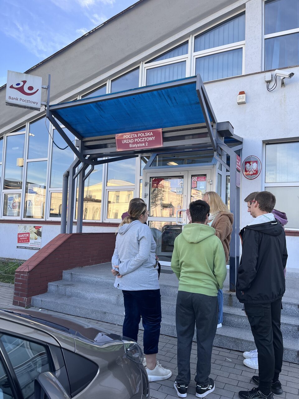 Wychowankowie wraz z wychowawczynią stoją przed budynkiem Poczty Polskiej.