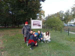 Wychowankowie pozują do zdjęcia ustawieni wokół tablicy upamiętniającej miejsce, gdzie stał w Białymstoku Hotel Ritz.
