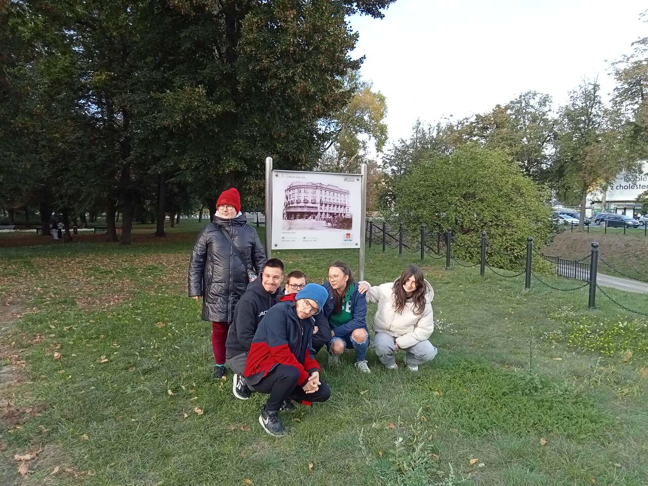 Wychowankowie pozują do zdjęcia ustawieni wokół tablicy upamiętniającej miejsce, gdzie stał w Białymstoku Hotel Ritz.
