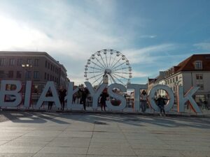 Młodzież pozuje do zdjęcia na tle Rynku Kościuszki w Białymstoku.
