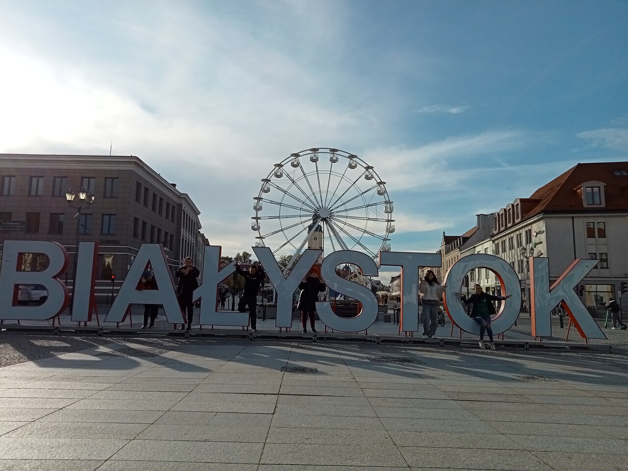 Młodzież pozuje do zdjęcia na tle Rynku Kościuszki w Białymstoku.
