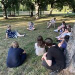 Młodzież wraz z wychowawcą relaksuje się na trawie pod drzewem.