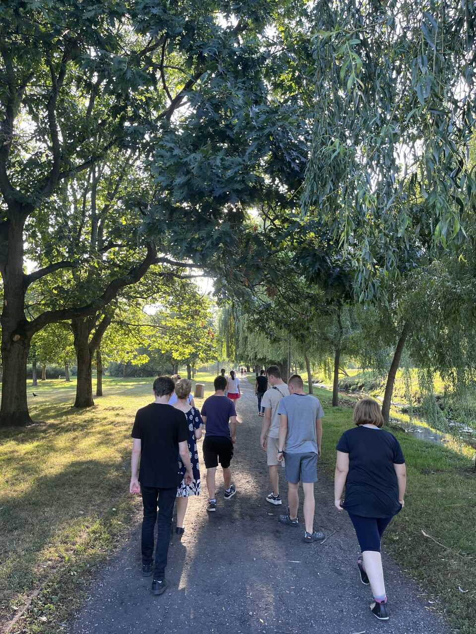 Młodzież z wychowawcą spaceruje ścieżką w parku.