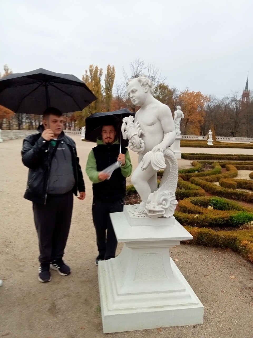 Dwóch wychowanków stoi przy rzeźbie przedstawiającej małego chłopca z rakiem w ręku.

