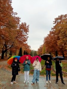 Młodzież stoi z otwartymi parasolami na tle jesiennego parku.
