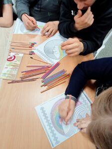 Na stole leżą kredki i kartki z rysunkami młodzieży
