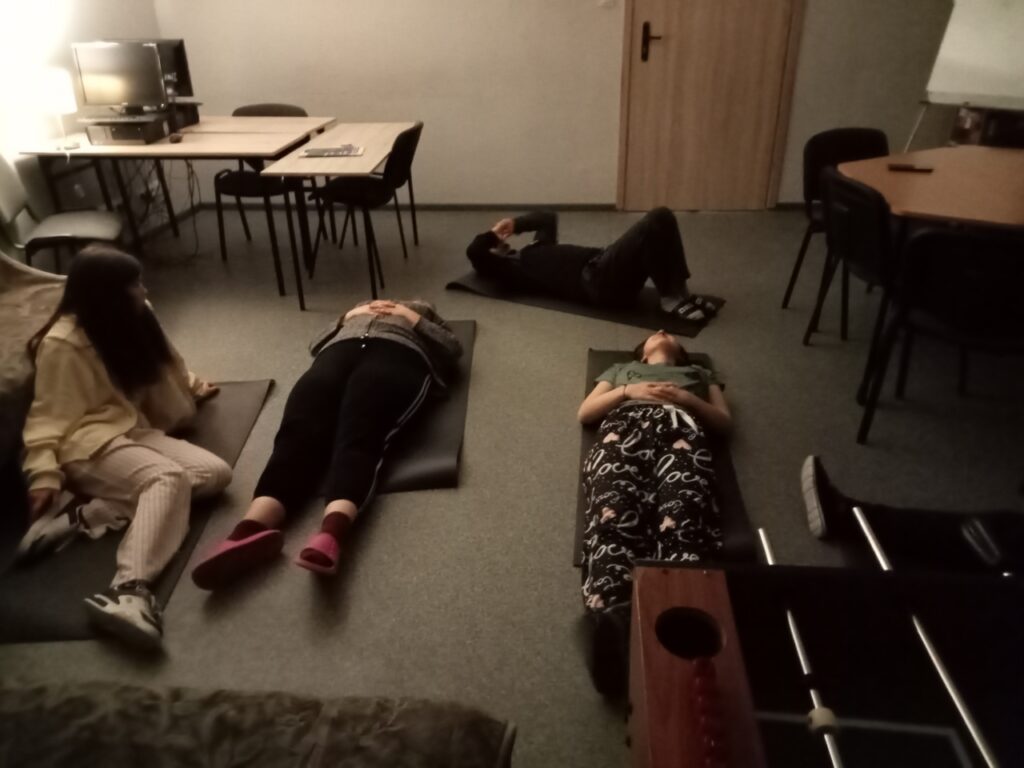 Młodzież leżąc na matach ćwiczy wdech i wydech przez nos.