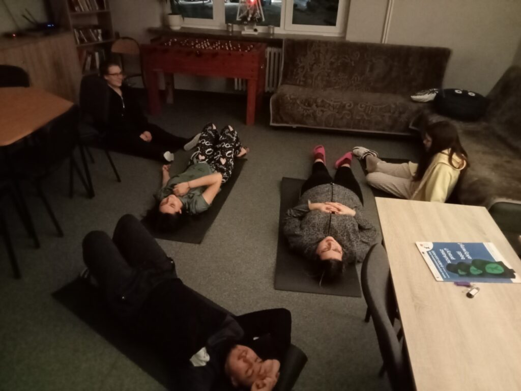 Młodzież leżąc na matach wykonuje ćwiczenia rozluźniające mięśnie.