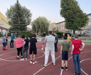 Zd.4
Młodzież bierze aktywny udział w grze piłki koszykowej na boisku szkolnym.