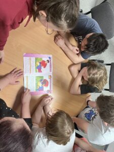 Zdj. 1. Pielęgniarka razem z wychowankami ogląda rysunek, na którym pokazane jest co po kolei robimy udzielając pierwszej pomocy osobie poszkodowanej.
