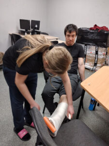 Dziewczyna zakłada chłopcu szynę i opatrunek usztywniający na nogę.