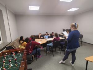 2. Wychowawczyni wyjaśnia zebranym wokół stołu uczestnikom zadanie do wykonania
