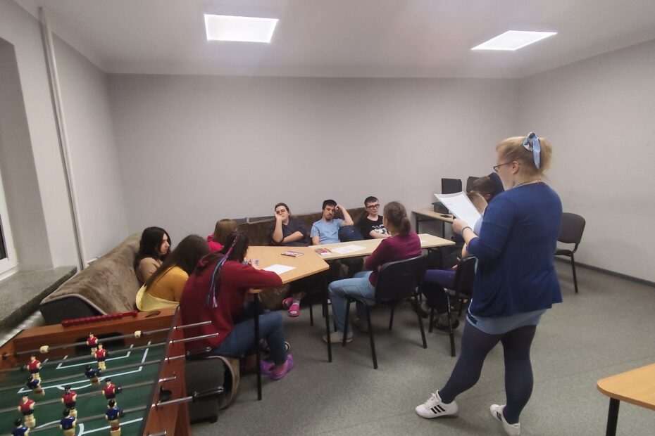 2. Wychowawczyni wyjaśnia zebranym wokół stołu uczestnikom zadanie do wykonania