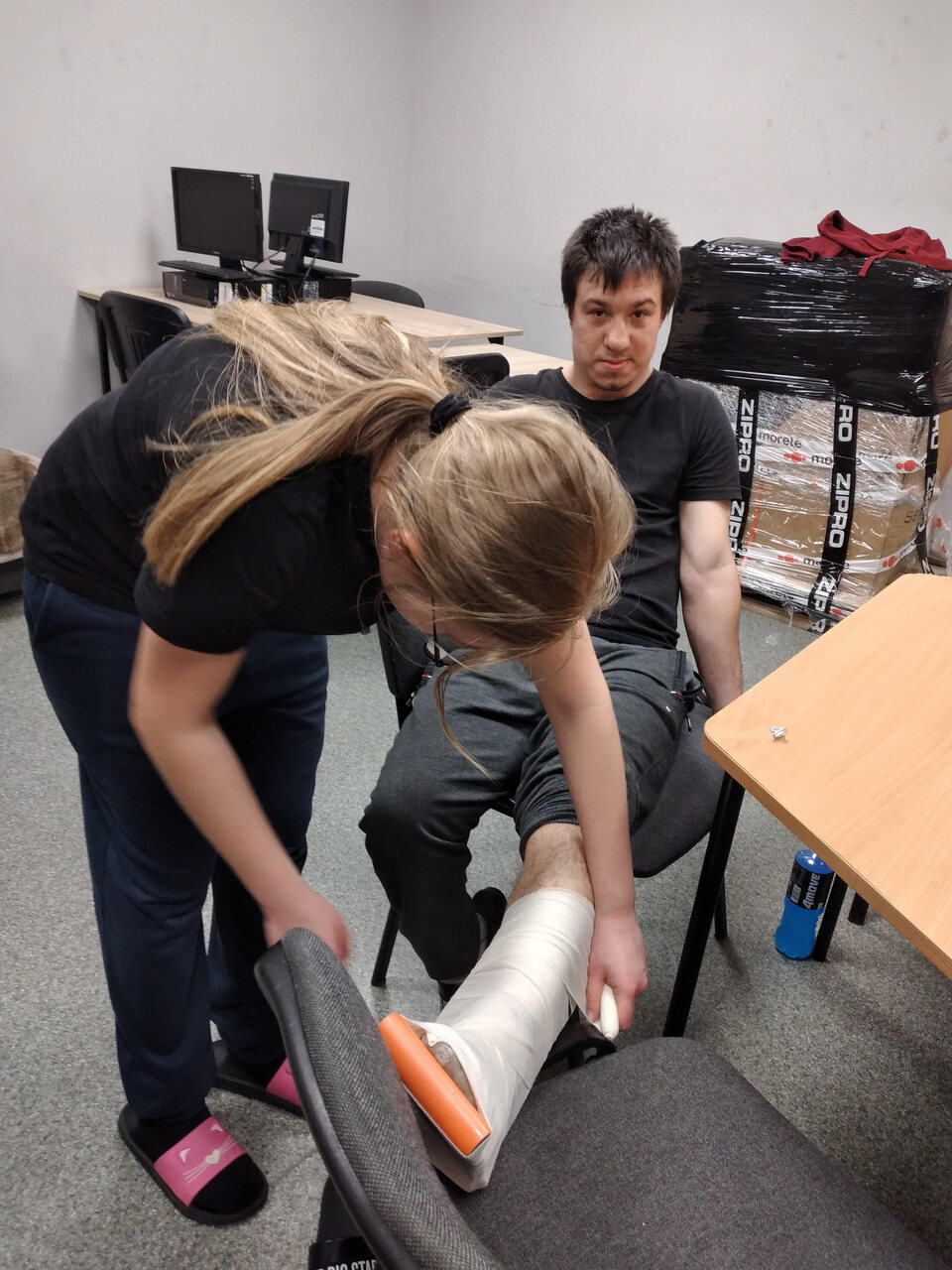 Dziewczyna zakłada chłopcu szynę i opatrunek usztywniający na nogę.