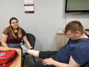 Koleżanka wykonuję koledze opatrunek usztywniający na nodze