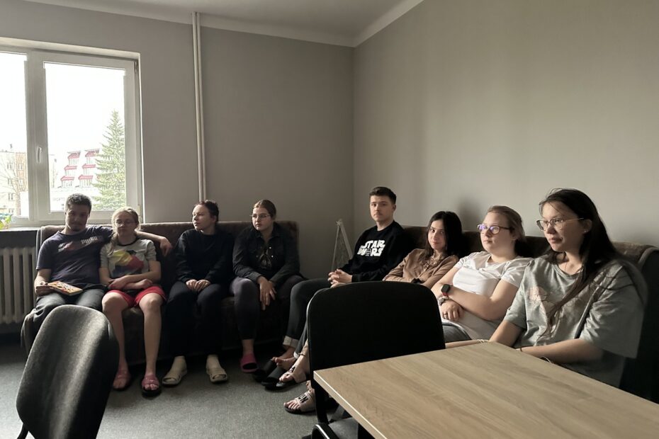 Na szarej kanapie w świetlicy internatu siedzi obok siebie ośmioosobowa grupa wychowanków; wszyscy zwróceni są w jedną stronę, jakby oglądali film, w pomieszczeniu jest półmrok, a z lewej strony widać okno z dziennym światłem.