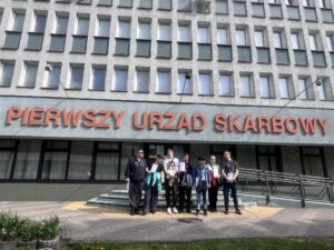 Zdj. 1 Wychowankowie stoją przed budynkiem Urzędu Skarbowego.





