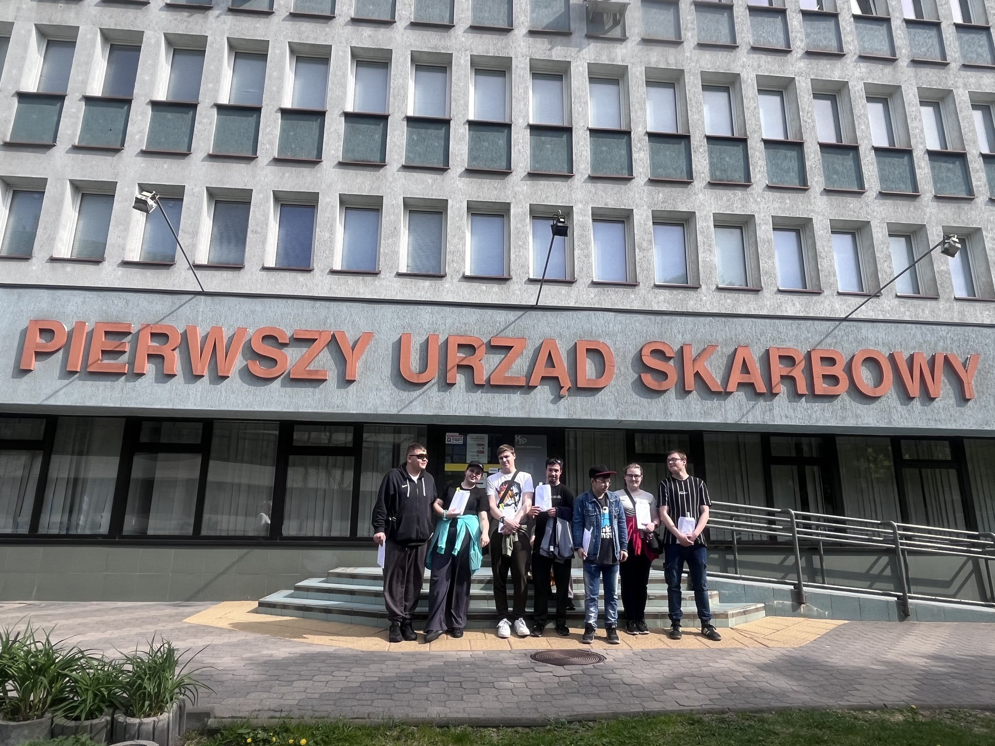 Zdj. 1 Wychowankowie stoją przed budynkiem Urzędu Skarbowego.





