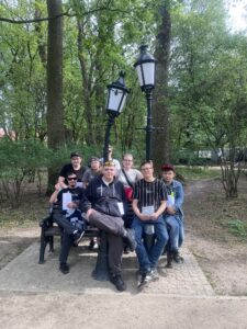 Zdj. 11 Wychowankowie uśmiechnięci siedzą na ławce w parku i pozują do wspólnego zdjęcia.