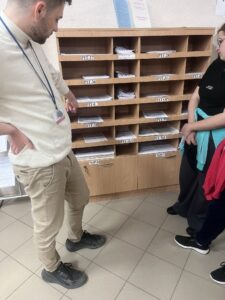 Zdj. 3 Pracownik urzędu pokazuje wychowankom półkę z dostępnymi drukami do wypełnienia.