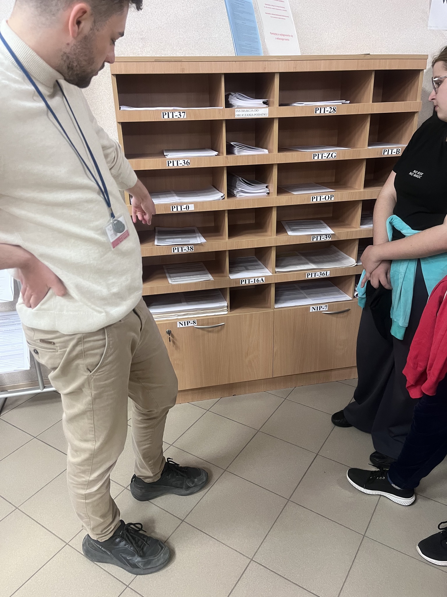 Zdj. 3 Pracownik urzędu pokazuje wychowankom półkę z dostępnymi drukami do wypełnienia.
