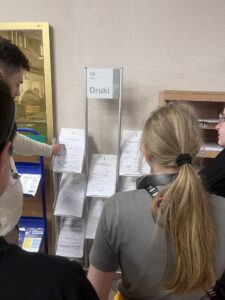 Zdj. 6 Pracownik urzędu pokazuje wychowankom półkę z dostępnymi drukami do wypełnienia.
