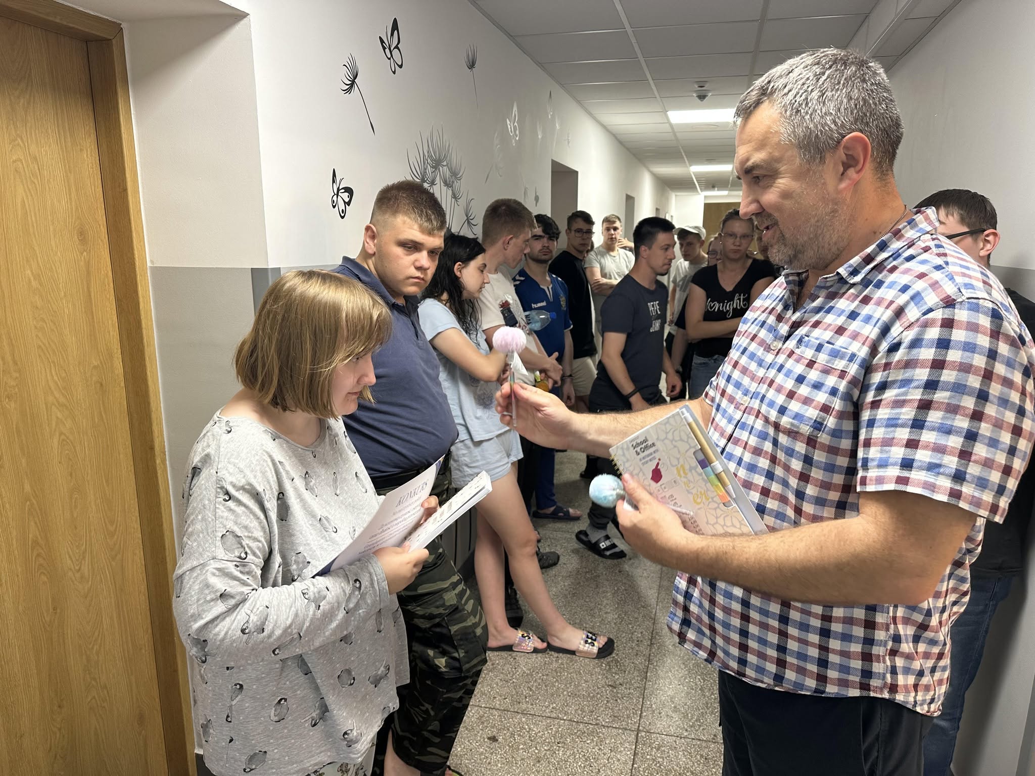 Zdjęcie 4
Wychowawca wręcza uczennicy nagrodę i dyplom podczas podsumowania konkursu.
W tle stoją inni mieszkańcy internatu, którzy przyglądają się temu wspaniałemu wydarzeniu.